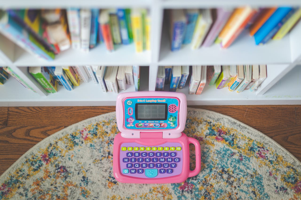 Colorful childrens toy laptop on a rug beside a bookshelf with colorful books.